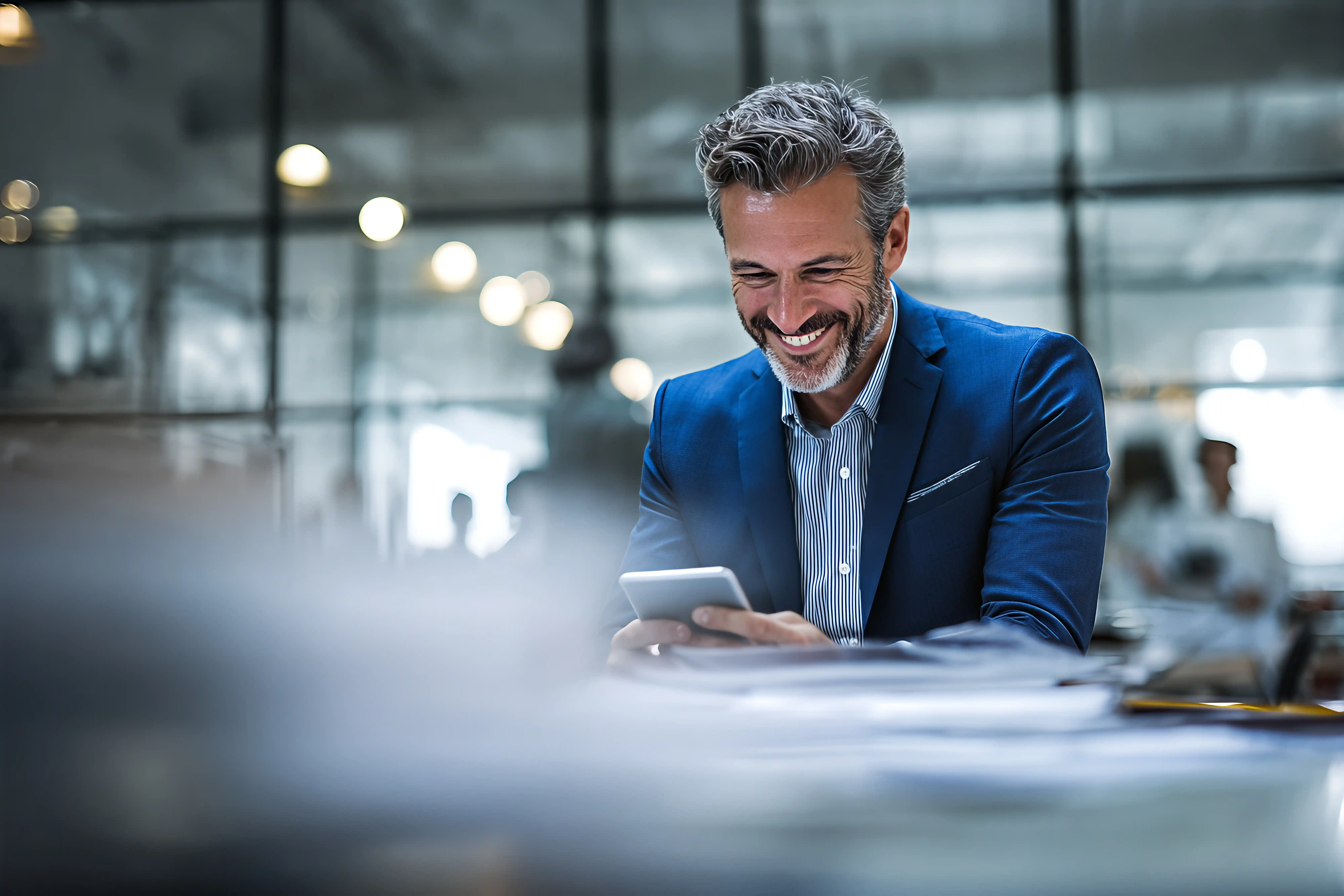 Professional man smiling while using a smartphone in a modern office environment.